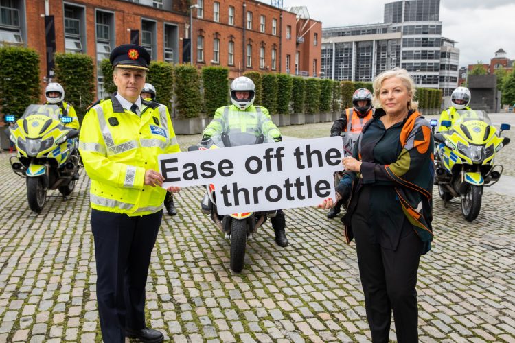 Liz O Donnell holding a banner saying Ease off the throttle as part of a motorcycle safety campaign